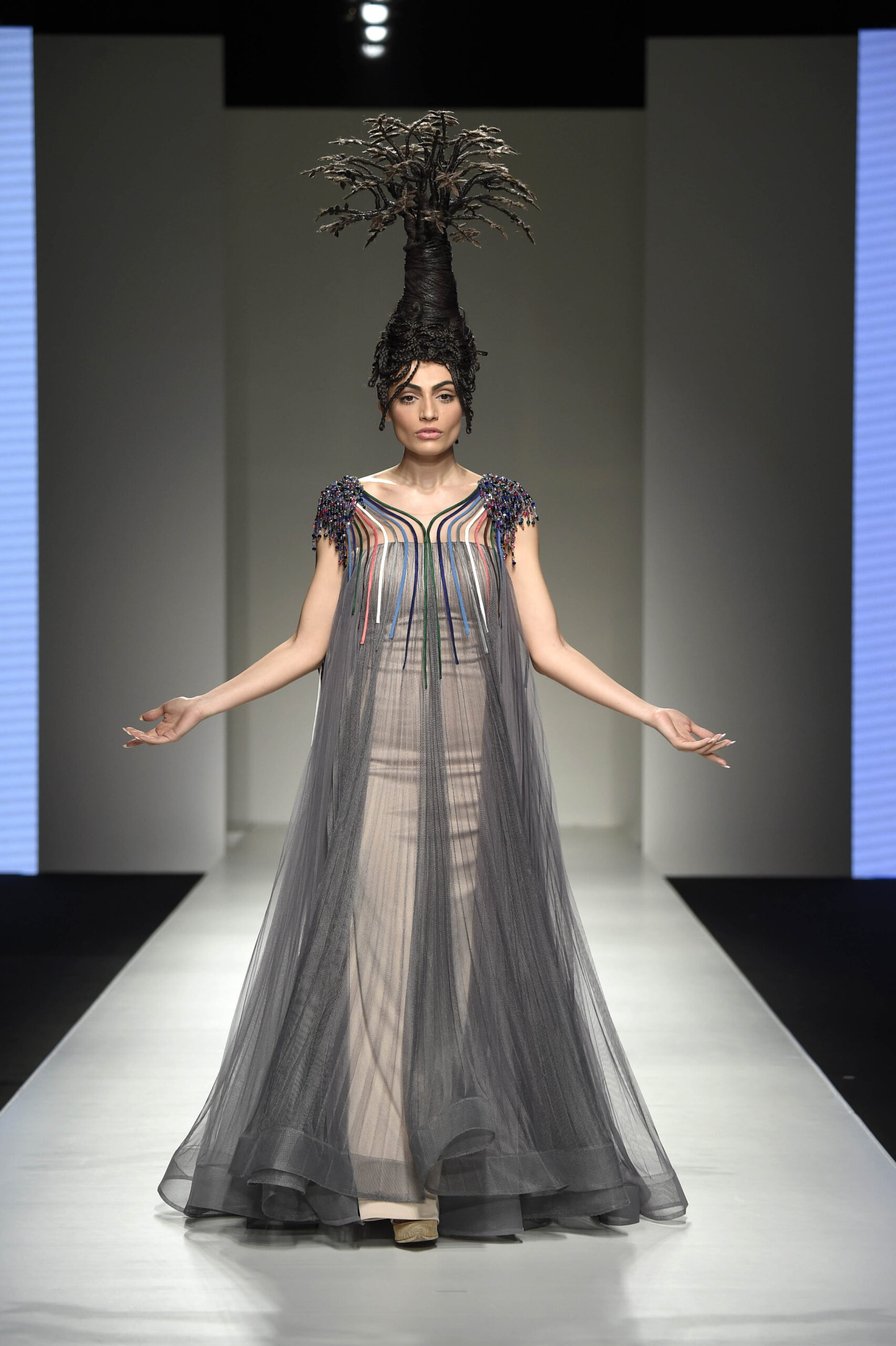 Model walking the runway at Arab Fashion Week, showcasing the "Tree of Life by Fadi Nasr, crafted using hair and a platform, paired with a sheer black gown.